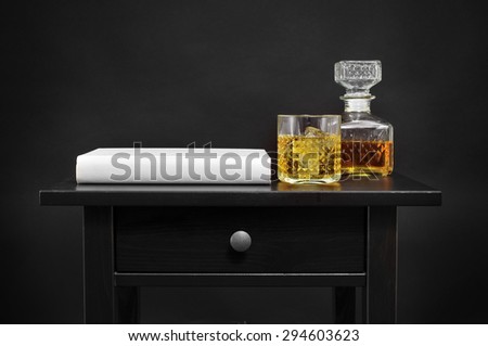a book, and a bottle and a lowball glass with liquor on a black table, over a black background