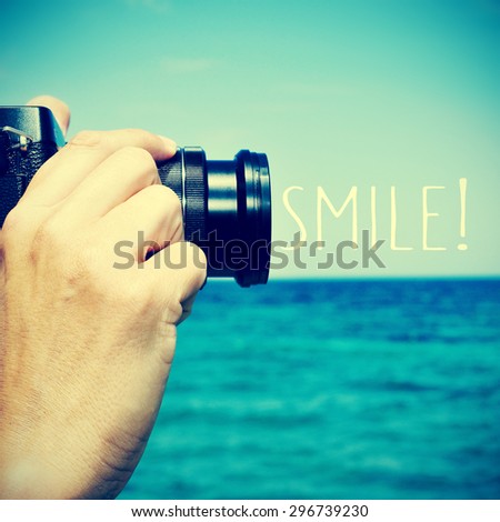 closeup of a young caucasian man taking a picture with a camera in front of the sea and the text smile!, with a retro effect