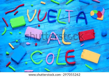 the sentence vuelta al cole, back to school in spanish, written with modelling clay of different colors, on a blue rustic wooden background