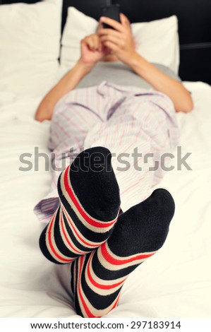 a young caucasian man wearing pajamas and colorful striped socks uses a smartphone in bed