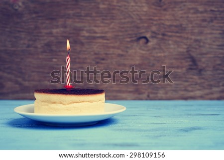 a cheesecake with a lighted birthday candle on a rustic blue wooden surface, with a retro effect