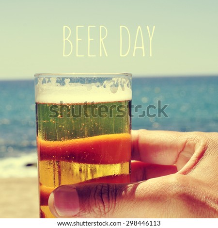 closeup of the hand of a man with a refrehing beer near the sea and the text beer day