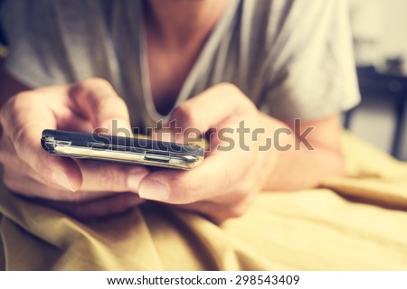 closeup of a young caucasian man in pajamas face down in bed using a smartphone