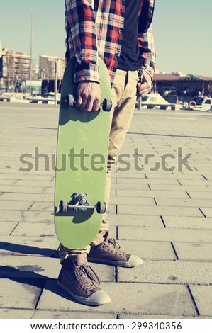 young caucasian man wearing a plaid shirt holds a green skateboard in his hand