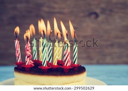 closeup of a cheesecake with some lighted birthday candles of different colors, with a retro effect