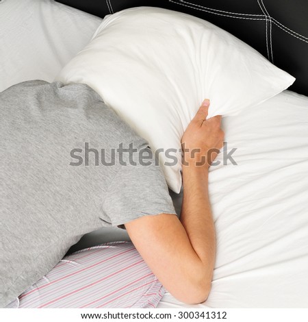 closeup of a young man face down in bed covering tightly his head with a pillow