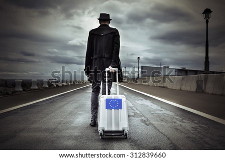 closeup of a young man seen from behind carrying his rolling suitcase with an European flag, with a dramatic effect