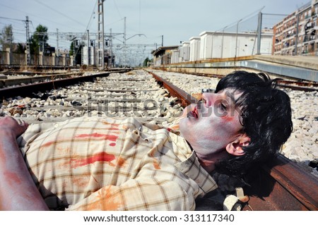 closeup of a scary zombie man lying down at the railroad tracks
