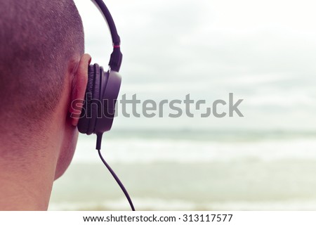 closeup of a young man listening to music with headphones in front of the sea, with a filter effect