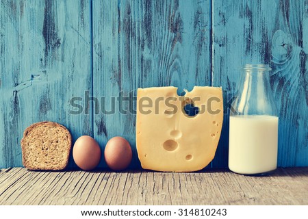 a toast, some eggs, a piece of Swiss cheese and a bottle with milk on a rustic wooden table, against a blue rustic wooden background, with a filter effect