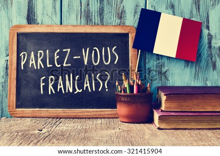 a chalkboard with the question parlez-vous francais? do you speak french? written in french, a pot with pencils and the flag of France, on a wooden desk
