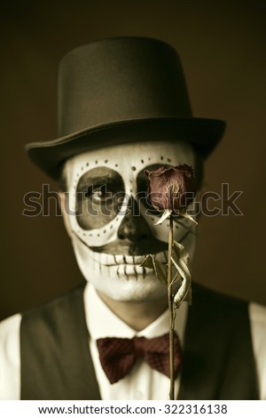 portrait of a young man with calaveras makeup, wearing bow tie and top hat, with a dry rose in front of his eye, with a vintage effect