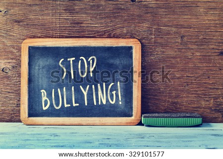 the text stop bullying written with chalk in a chalkboard and an eraser on a blue rustic wooden desk in a classroom