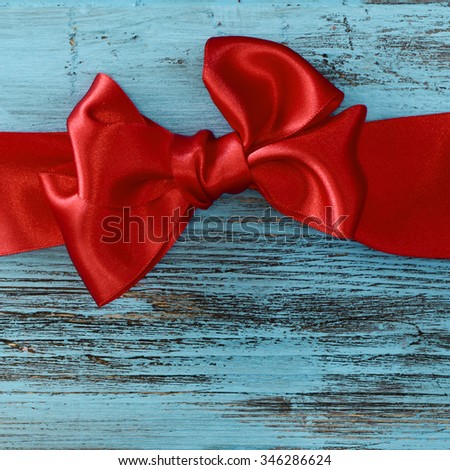 a red satin ribbon bow on a blue rustic wooden surface