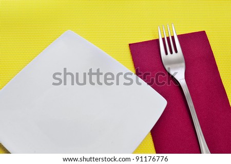 a dinner set formed by a fork, a plate and a napkin on a yellow tablecloth