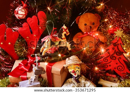 some gifts and some retro toys, such as a teddy bear, a horse or a marionette, under a christmas tree ornamented with lights, balls and tinsel