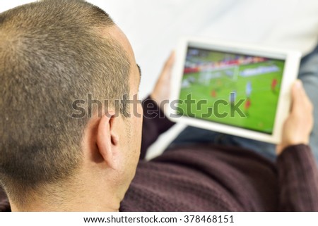 a young man lying on the couch watches a soccer match in streaming in his tablet computer