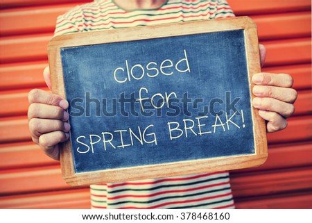 closeup of a young caucasian man showing a chalkboard with the text closed for spring break, outdoors, against an orange background