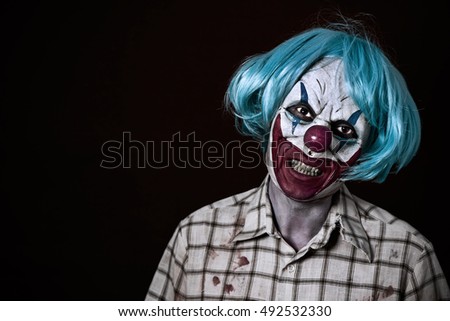 portrait of a scary evil clown wearing a ragged and dirty shirt with blood stains and a blue wig, against a dark background
