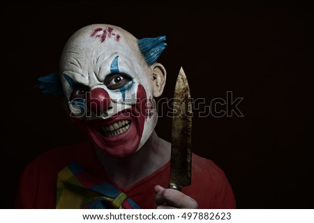 a scary evil clown with a big knife in his hand, against a dark background