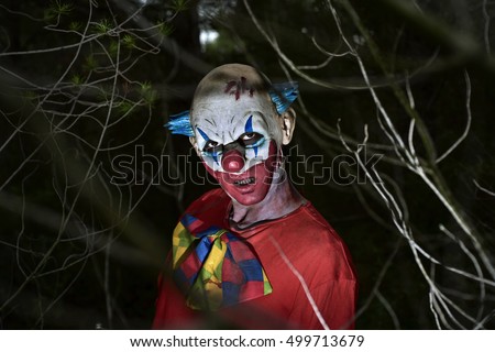 closeup of a scary evil clown in the woods, in the dark of night