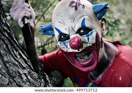 a scary evil clown with a big knife in his hand in the woods