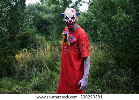 a scary evil clown, wearing a dirty costume, in the woods