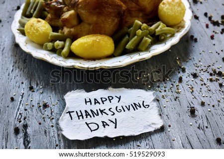 a piece of paper with the text happy thanksgiving day handwritten in it and a roast turkey on a round ceramic tray, placed on a rustic wooden table