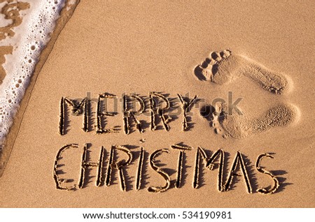 some foot prints and the text merry christmas written in the sand of a beach