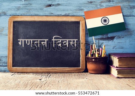 a chalkboard with the text Republic Day written in Hindi and a flag of India, on a rustic wooden surface, against a blue wooden background