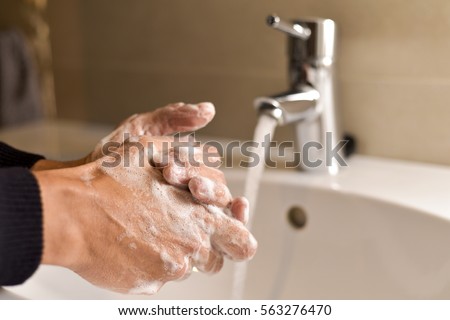 closeup of a young caucasian man washing his hands with soap in the sink of a bathroom