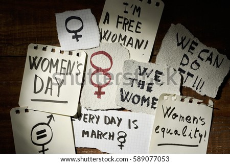 closeup of many pieces of paper with concepts relative to the womens day written in it, such as womens equality, we the women, we can do it or every day is march 8, on a rustic wooden surface
