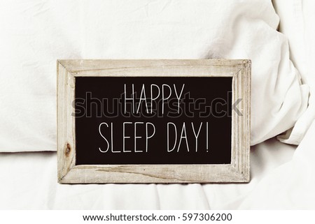 closeup of a wooden-framed chalkboard with the text happy sleep day written in it, placed on a comfortable bed
