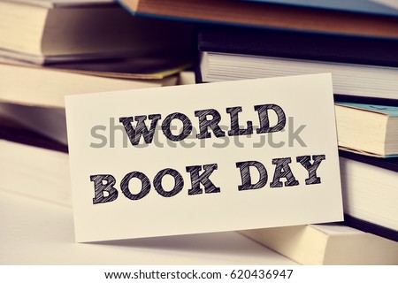 closeup of a piece of paper with the text world book day in front of a pile of books, placed on a white surface