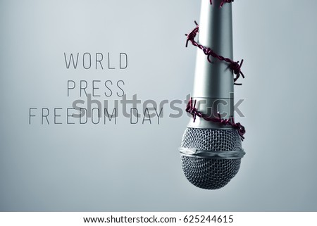 closeup of a microphone encircled by a red barbed wire and the text world press freedom day on a gradient gray background