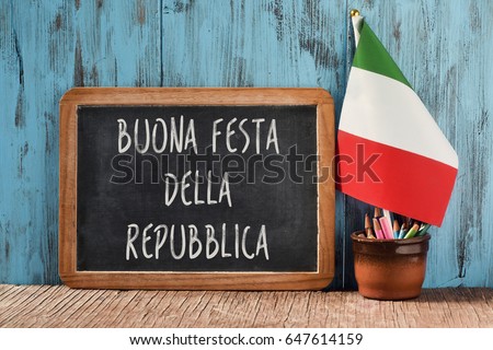 the text buonna festa della repubblica, happy republic day, the national day of italy, written in italian in a chalkboard, and a flag of italy, on a rustic wooden table
