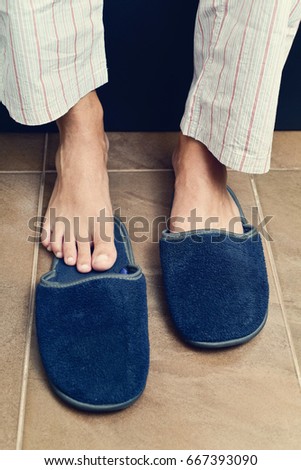 closeup of a young caucasian man in pajamas sitting on the edge of the bed putting on or putting off a pair of warm slippers