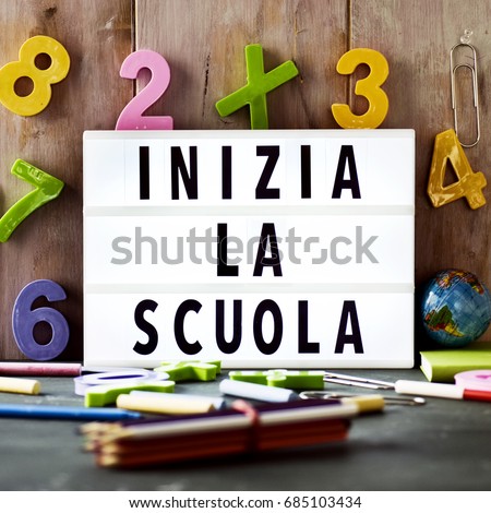 the text inizia la scuola, back to school in italian, in a lightbox placed against a rustic wooden background, surrounded by three-dimensional numbers and chalks and pencils of different colors