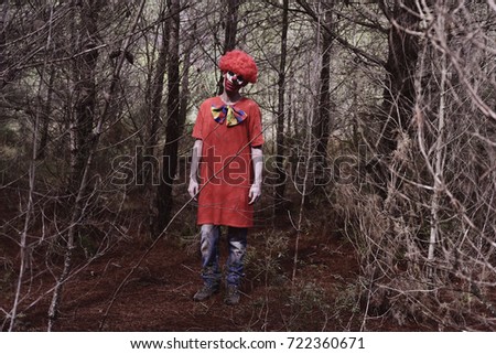 a scary evil clown wearing a red wig and a dirty costume, in the woods