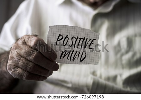 closeup of an old caucasian man with a note in his hands with the text positive mind written in it