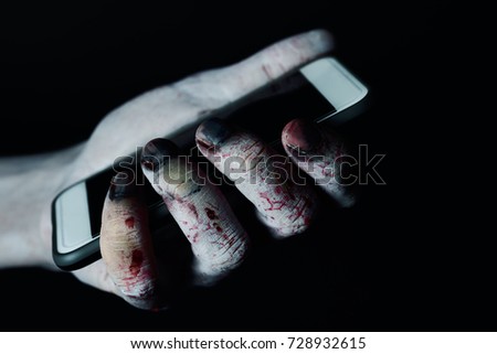 closeup of a scary and bloody hand holding a smartphone against a black background