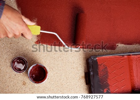 hihg-angle shot of a young caucasian man painting red a wooden board with a paint roller