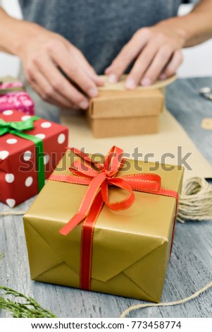 closeup of a young caucasian man wrapping a gift on a gray rustic table full of gifts wrapped in papers with different patterns and tied with ribbons of different colors