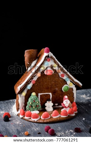 a messy homemade gingerbread house on a rustic wooden table, againt a black background with a blank space on top