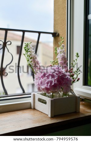 closeup of a bouquet of different pale pink flowers in a wooden box placed on a window sill