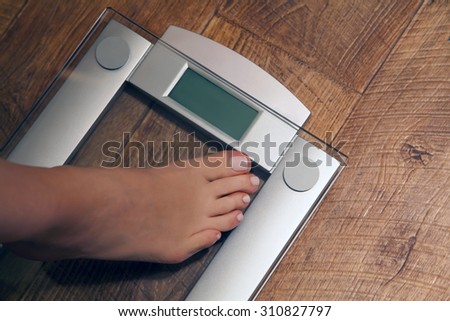 Woman's feet stepping on weight scale. Close-up. Dieting concept.