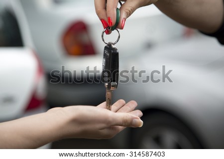 Close up of woman receiving car key from car salesperson of a new car she has bought.