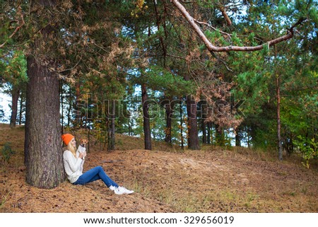 girl sits under a tree in the forest and keeps the dog in her arms