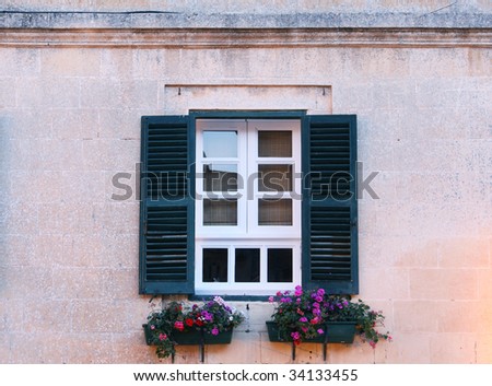 a typical maltese window with louvered shuters and square paned windows with flowers in hanging flower pots