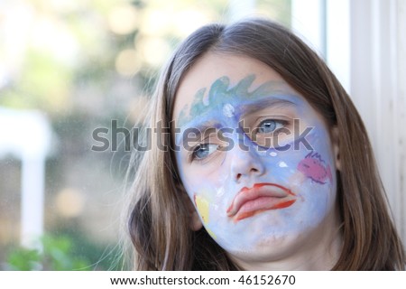 portrait of an upset caucasian child with her face painted looking away from the camera